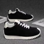 Black sneakers with white laces and chunky off-white soles on a gray background